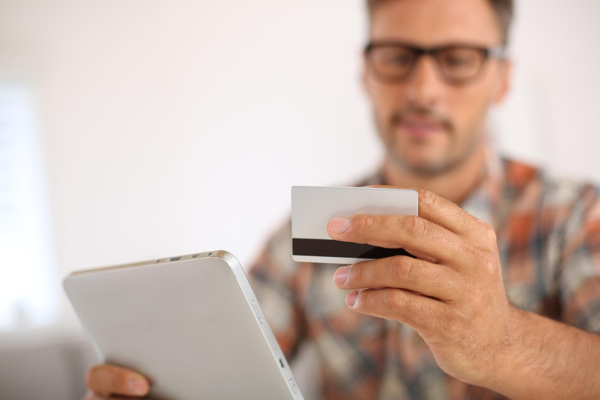 Man looking at numbers on his credit card while holding a tablet.