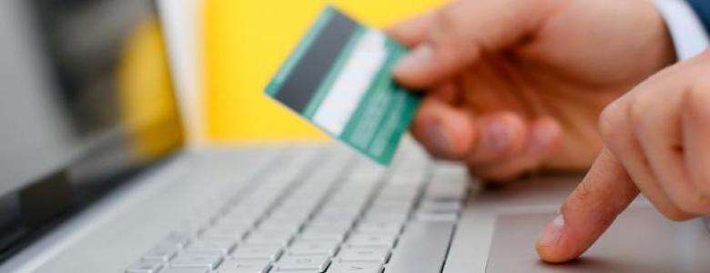 Man typing on laptop while holding credit card