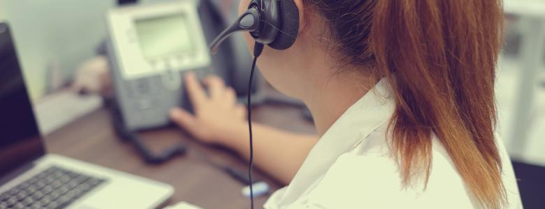 Lady sitting in front of a computer wearing a headset and writing in a notebook