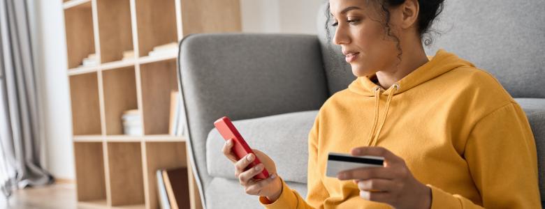 Woman in yellow jumper holding phone and debit card.